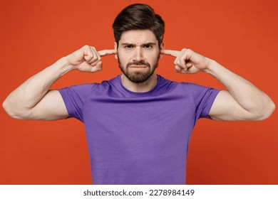 Young dissatisfied annoyed caucasian man wears casual basic purple t-shirt closed eyes cover ears with hands fingers do not want to listen scream isolated on plain orange background studio portrait