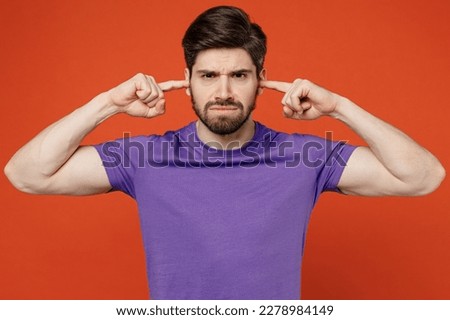 Young dissatisfied annoyed caucasian man wears casual basic purple t-shirt closed eyes cover ears with hands fingers do not want to listen scream isolated on plain orange background studio portrait