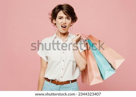 Young dissatisfied displeased woman wearing casual clothes hold shopping paper package bags look camera isolated on plain light pastel pink color background studio. Black Friday sale buy day concept