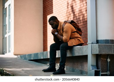 Young distraught African American student sitting at campus and thinking of something.