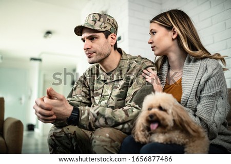 Young distraught military couple with a dog at home. Woman is consoling her husband while he is about to leave for deployment. 