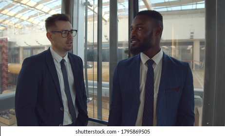 Young diverse colleagues smiling and chatting lifting in glass elevator. Multiethnic business partners discussing financial project taking elevator in office building - Powered by Shutterstock