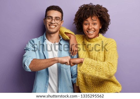 Young diverse couple give fist bump, agree to bring plan to life, smile broadly, have mixed race relationships, have good friendly partners, isolated over purple wall. I agree with you concept