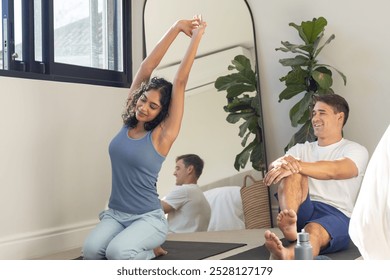 Young diverse couple practicing yoga together at home in bright room. Large window with indoor plants creating a peaceful background, unaltered - Powered by Shutterstock