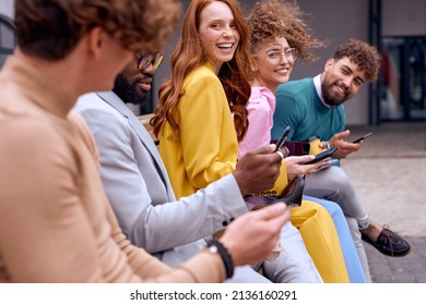 young diverse coworkers during break time outside of office, sitting on bench having fun using modern smartphone, dressed in fashionable elegant clothes, enjoy spare time, have conversation and laugh - Powered by Shutterstock