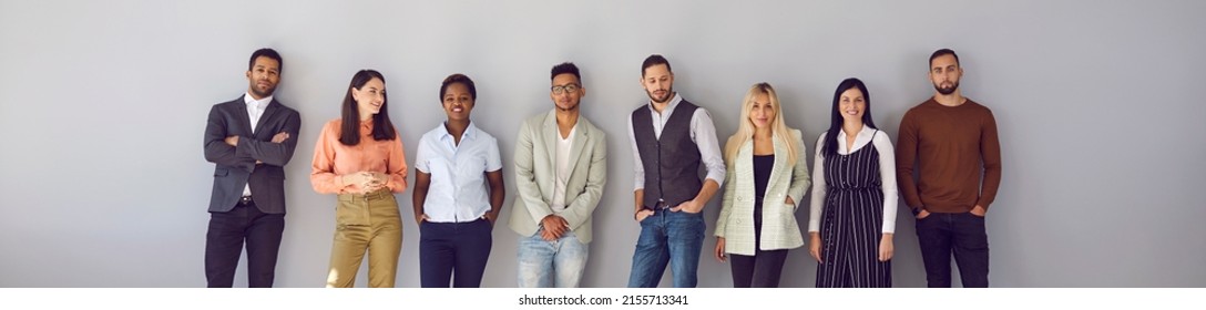 Young diverse fashion models posing against gray background. Banner with group portrait of confident young multi ethnic people in smart casual office wear standing in studio and leaning on grey wall - Shutterstock ID 2155713341