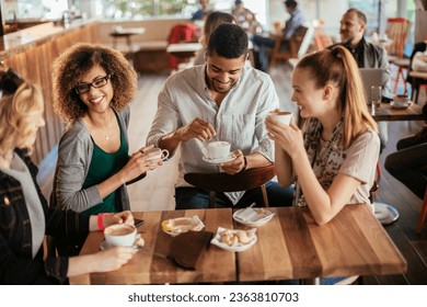 Young and diverse group of friends having a conversation over some coffee and desserts in a cafe - Powered by Shutterstock