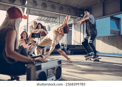 Young and diverse group of people breakdancing and filming it on a smartphone in a parking lot - Powered by Shutterstock