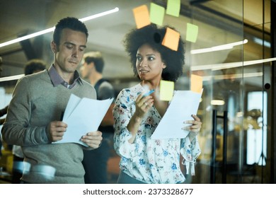 Young and diverse group of people going over ideas for a project and putting notes on a window in a startup company office