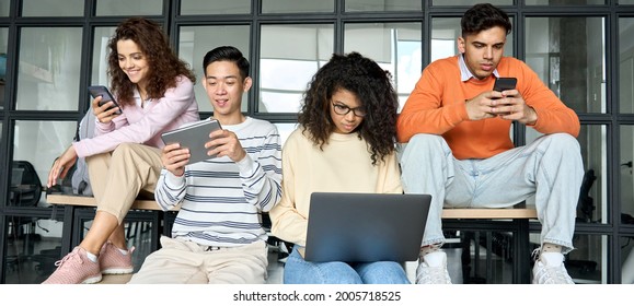 Young diverse multiracial cool group of high school college students girls and guys sitting at university campus space holding technology gadgets using digital devices studying together. - Shutterstock ID 2005718525