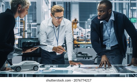 Young Diverse Team Of Automotive Engineers Working In Office At Car Factory. Industrial Designer Talks About Electric Engine Parts With Colleagues, Discussing Different Technological Applications.