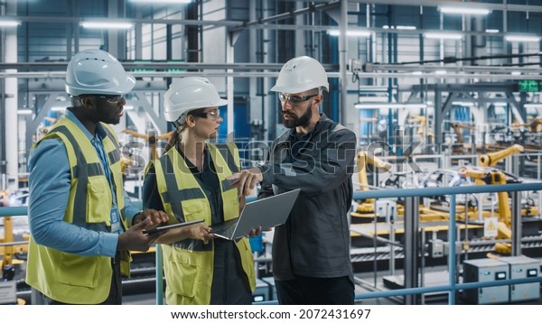 Young Diverse Team of Car Factory Specialists\
Working on Laptop and Tablet Computers. Engineers Discussing\
Automotive Industrial Manufacturing Technology on Modern Vehicle\
Assembly Plant.