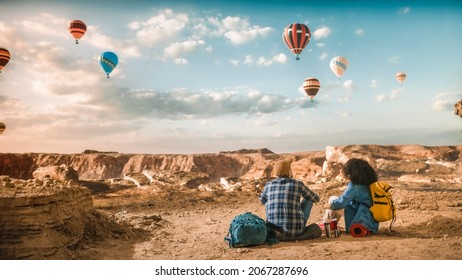 Young Diverse Tourist Couple Hiking with Backpacks, Resting on Top of Rocky Canyon Valley. Male and Female Backpacker Friends on Adventure Trip. Hot Air Balloon Festival in Mountain National Park. - Powered by Shutterstock