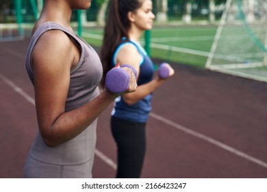 Young Diverse Women Pump Arm Muscles With Dumbbells In The Outdoor Stadium. Close Up