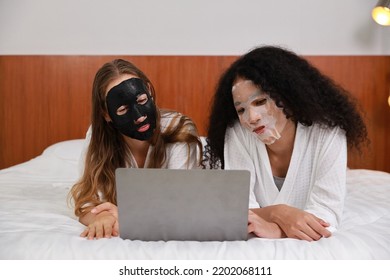 Young Diversity Ethnic Beautiful Woman In Bathrobe Playing Social Media On Computer While Doing Cosmetic Facial Mask For Skin Care And Treatment. Women Lesbian Couple Daily LGBTQ Lifestyle Concept.