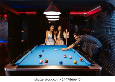 Young diversity group of people playing pool together with smile, enjoyment and fun. Young people spend time in billiards room at the nightclub. Men, women friends playing billiards. Nightlife concept