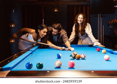 Young diversity group of people playing pool together with smile, enjoyment and fun. Young people spend time in billiards room at the nightclub. Men, women friends playing billiards. Nightlife concept