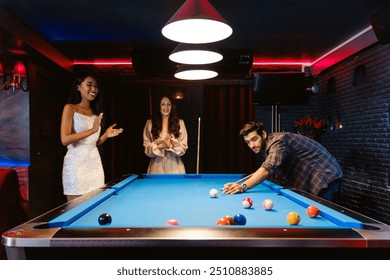 Young diversity group of people playing pool together with smile, enjoyment and fun. Young people spend time in billiards room at the nightclub. Men, women friends playing billiards. Nightlife concept