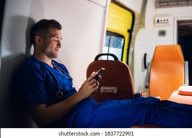 Young Doctor In A Blue Uniform Resting And Chatting With Someone Over The Phone At Night.