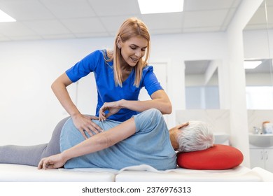 Young doctor chiropractor or osteopath fixing lying senior woman back with hands movements during visit in manual therapy clinic. Professional chiropractor during work - Powered by Shutterstock