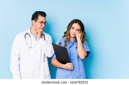 Young doctor couple posing in a blue background isolated who feels sad and pensive, looking at copy space.