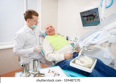 Young Doctor Dentist And Old Senior Man Patient, Smiling And Looking At The Camera