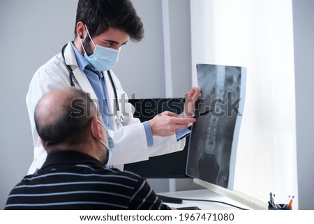Young doctor examining x-ray of a senior patient backbone. Radiography of a spine, spinal or vertebral column.