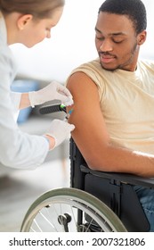 Young Doctor Giving Injection Of Coronavirus Vaccine To Handicapped Black Man In Wheelchair At Home. Impaired African American Guy Receiving Protection Against Covid. Community Vaccination