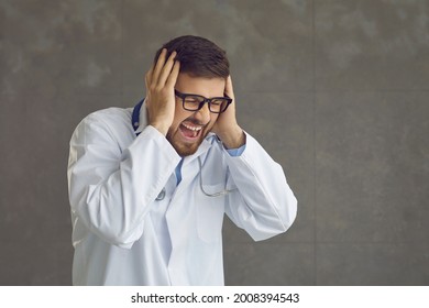 Young Doctor Going Mental. Studio Portrait Of Angry Frustrated Mad Crazy Furious Stressed General Practitioner Screaming And Closing Ears With Hands On Gray Copy Space Background