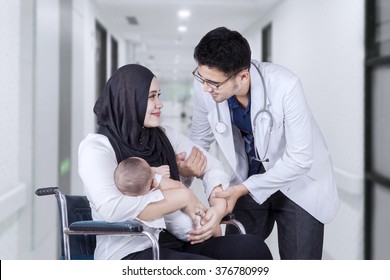 Young doctor help a young mother and her baby to stand from wheelchair in the hospital alley