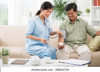 Young Doctor Helping Senior Man To Check Blood Pressure At Home