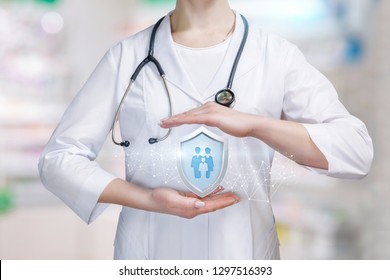 A Young Doctor Is Holding A Big Shield With Group Of People Or Family Members Icon Inside Between Her Palms In Protective Gesture. The Family Medicine And Life And Health Insurance Concept.