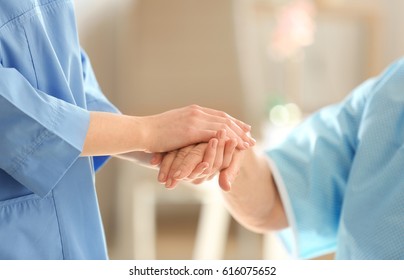 Young doctor holding hand of elderly woman on light background, closeup