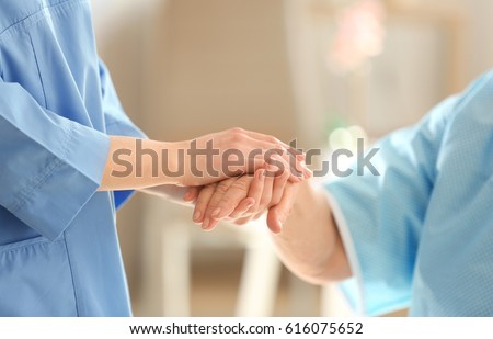 Young doctor holding hand of elderly woman on light background, closeup