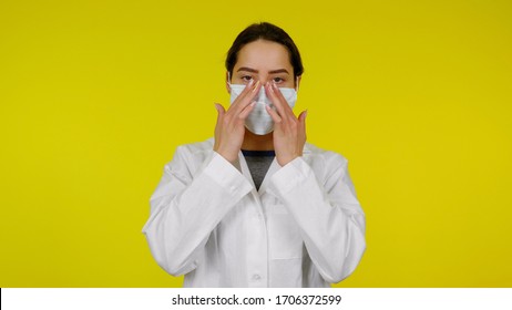 Young doctor infectious disease specialist adjusts a protective medical mask on her nose. Girl in a white coat against the yellow background puts on a mask on face, covering her nose and mouth - Powered by Shutterstock