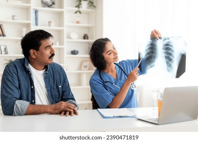 Young Doctor Lady Demonstrating Chest X-Ray To Mature Male Patient During Meeting In Clinic, Female Therapist In Uniform Consulting Ill Man During Appointment In Hospital, Discussing Treatment - Powered by Shutterstock