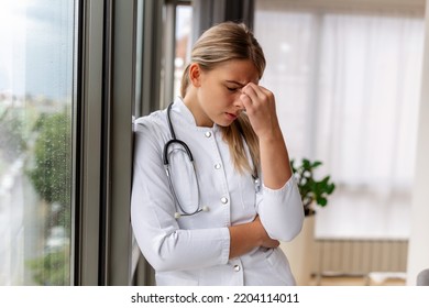 Young Doctor Looking Distressed. Tired Exhausted Female Doctor In Uniform At Hospital Holding Her Head. Depressed Sad Doctor Feels Burnout Stress