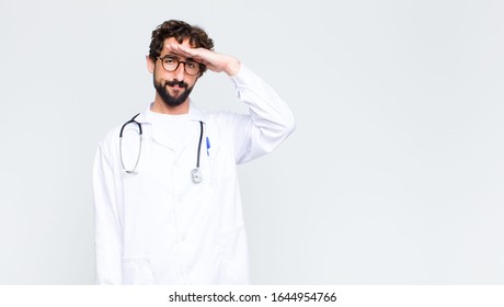 Young Doctor Man Greeting The Camera With A Military Salute In An Act Of Honor And Patriotism, Showing Respect Against Copy Space Wall