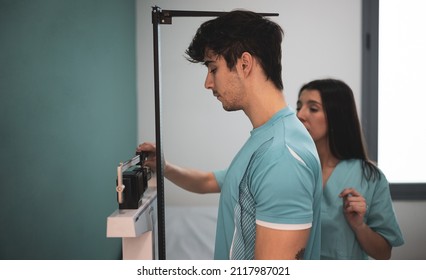 A Young Doctor Measures A Young Athlete On A Scale With A Height Meter In A Clinic.