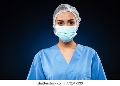 Young Doctor In Medical Mask And Cap Wearing Blue Uniform And Looking Camera Isolated Over Black