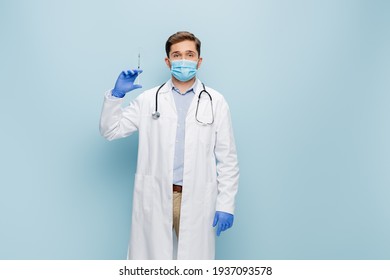 young doctor in medical mask and white coat with stethoscope holding syringe on blue