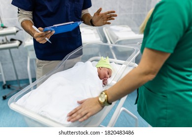 Young Doctor And Nurse Working In Maternity Ward. They Are Collecting Data, Measuring Weight And Wrapping The Newborn Baby.