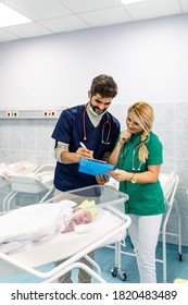 Young Doctor And Nurse Working In Maternity Ward. They Are Collecting Data, Measuring Weight And Wrapping The Newborn Baby.