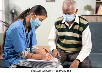 Young doctor or nurse writing prescription during home visiting to sick elder man while both worn face mask due to coronavirus covid-19 pandemic