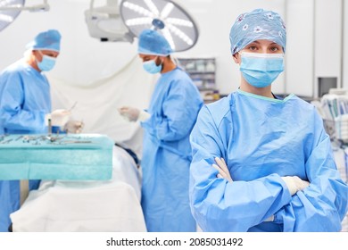 Young doctor or operating room nurse with crossed arms in operating room with surgery team and patient