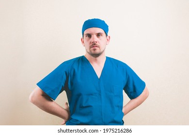 Young Doctor Portrait With Hands On Hips In Blue Surgeon Suit And Protective Breathing Mask On The Yellow Background Isolated