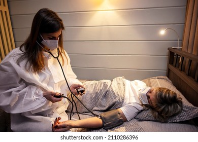 A Young Doctor In A Protective Mask Measures A Patient's Blood Pressure. A Doctor's Overnight Visit To A Patient.