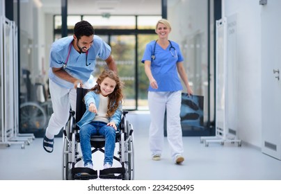 Young doctor pushing little girl at wheelchair at pediatric corridor, having fun. - Powered by Shutterstock