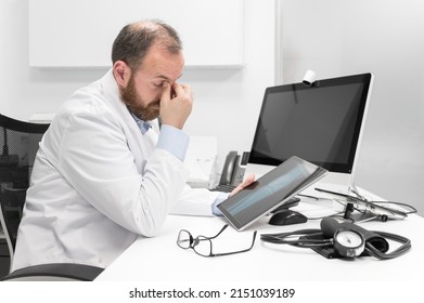 Young Doctor Rubbing His Eyes, Feeling Tired And Unhappy. Health Care Worker Stress And Frustration Concept. High Quality Photography