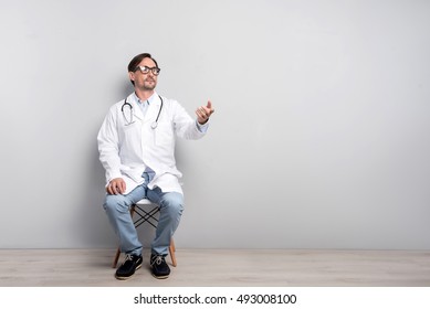 Young Doctor Sitting On A Grey Background